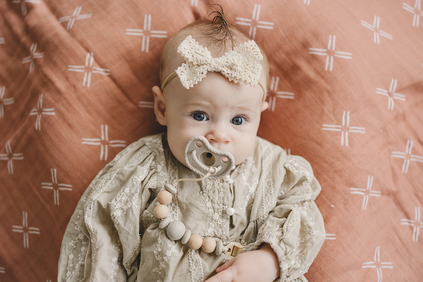 Baby in lace dress using Mila & Lulu Hazel round silicone pacifier with muslin and beaded clip