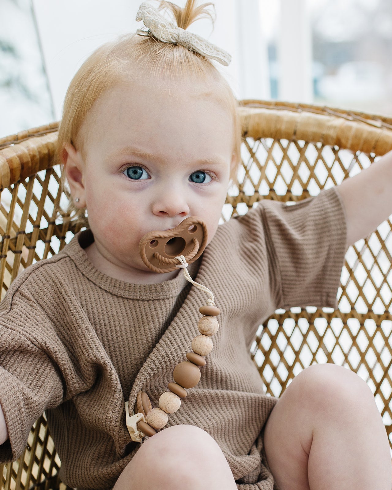 Baby in a wicker chair using a Mila & Lulu brown silicone pacifier with beaded wood pacifier clip