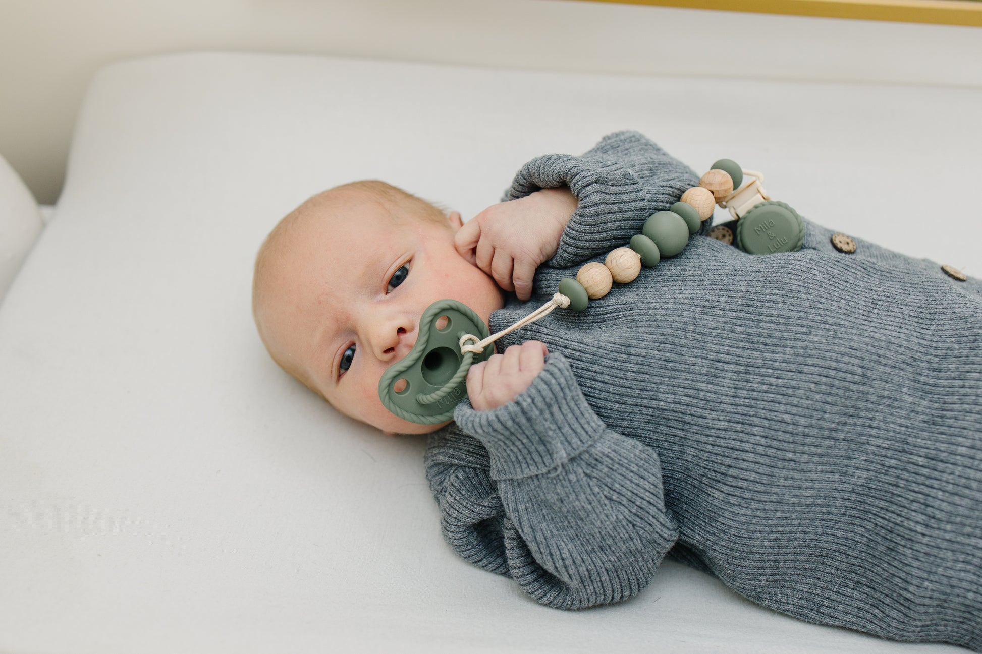 Newborn in gray knit outfit using Mila & Lulu sage round silicone pacifier with beaded wood clip